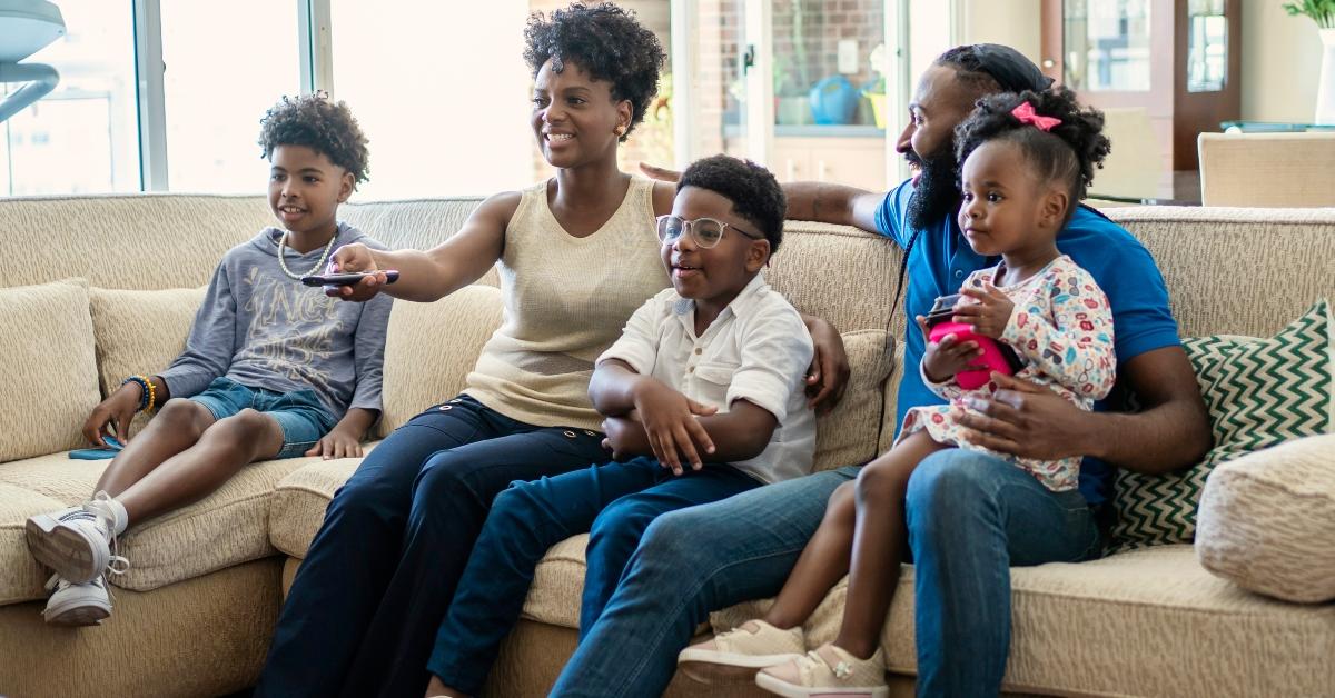 A family of five watches TV on the couch. 