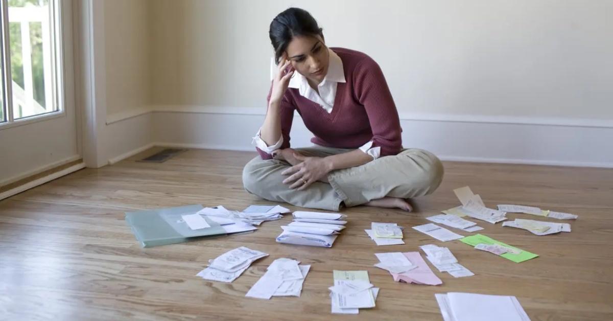 A woman in a burgundy sweatshirt sits around a pile of receipts saved for taxes.