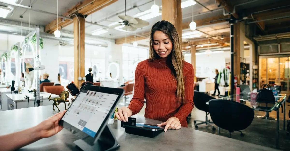 A woman in a red sweater swipes her credit card at the hair salon.