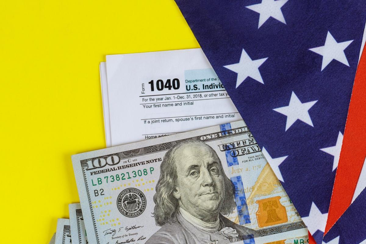 Form 1040, a $100 bill, and an American flag