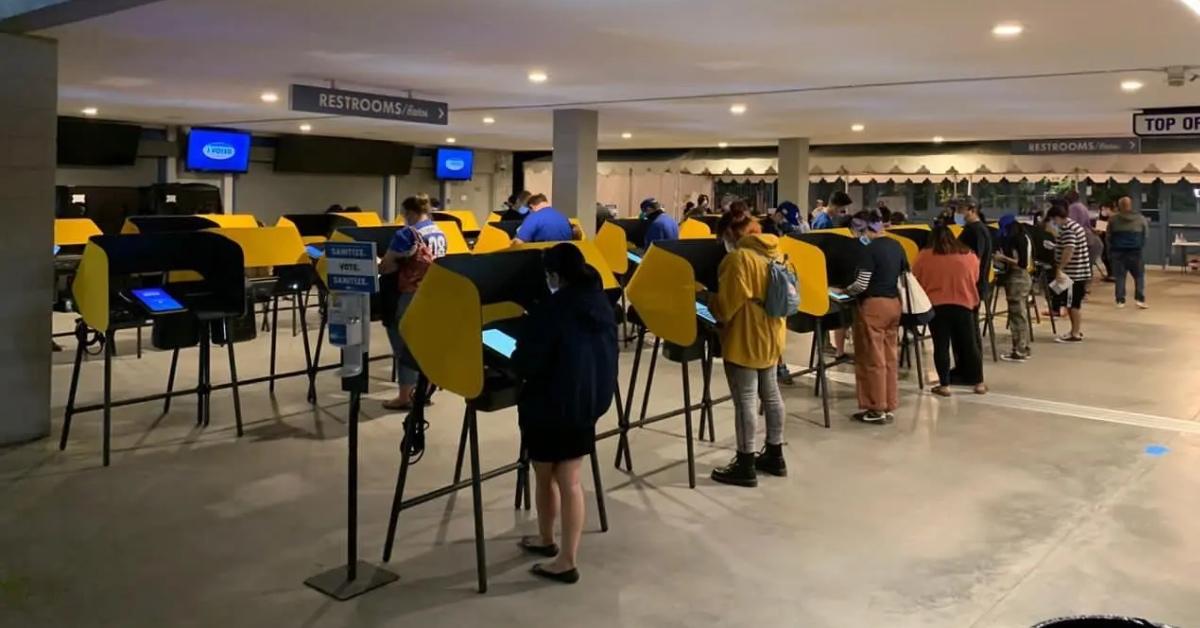 People standing in private yellow booths casting their votes on a Smartmatic voting machines.