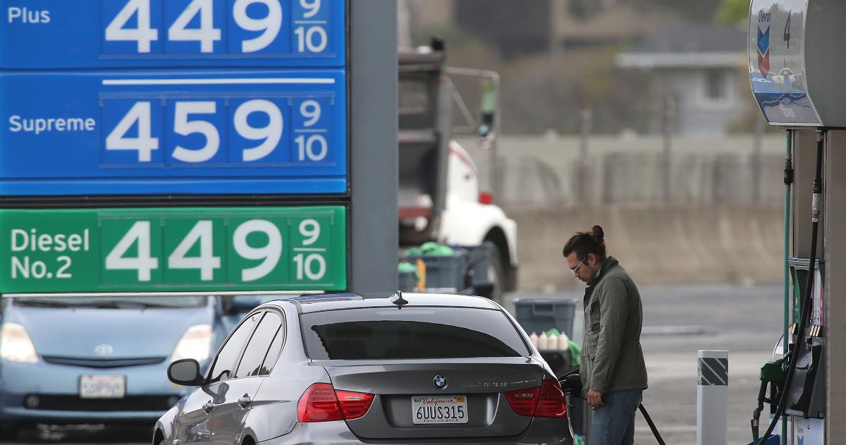 A  man pumping gas in front of a gas price sign