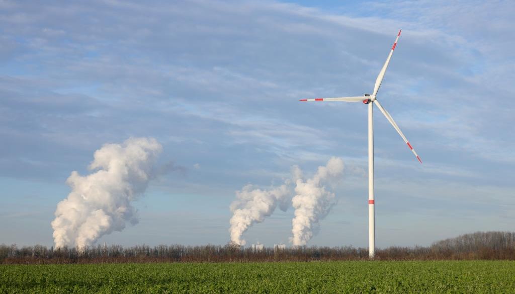 A wind turbine in front of a power plant