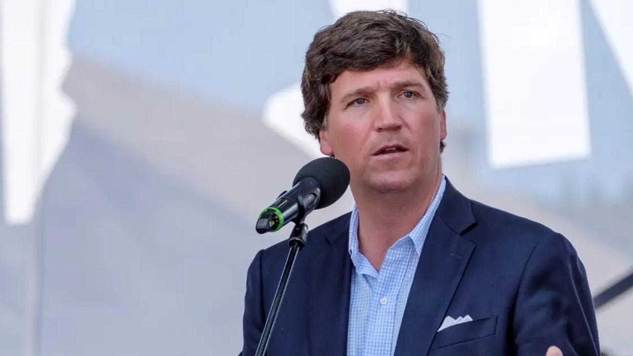 Tucker Carlson speaking into a microphone and wearing a blue suit