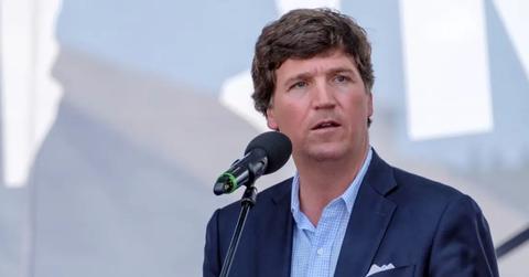 Tucker Carlson speaking into a microphone and wearing a blue suit