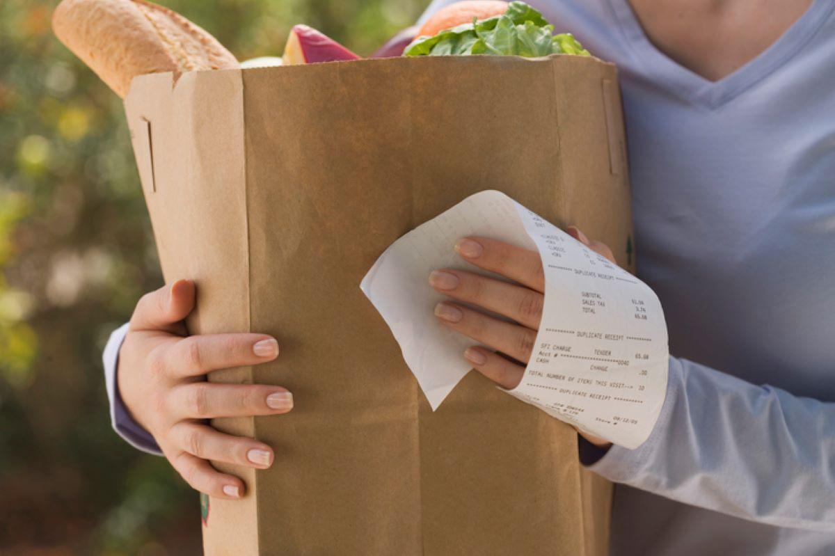 Woman walking with a paper grocery bag and receipt in hand