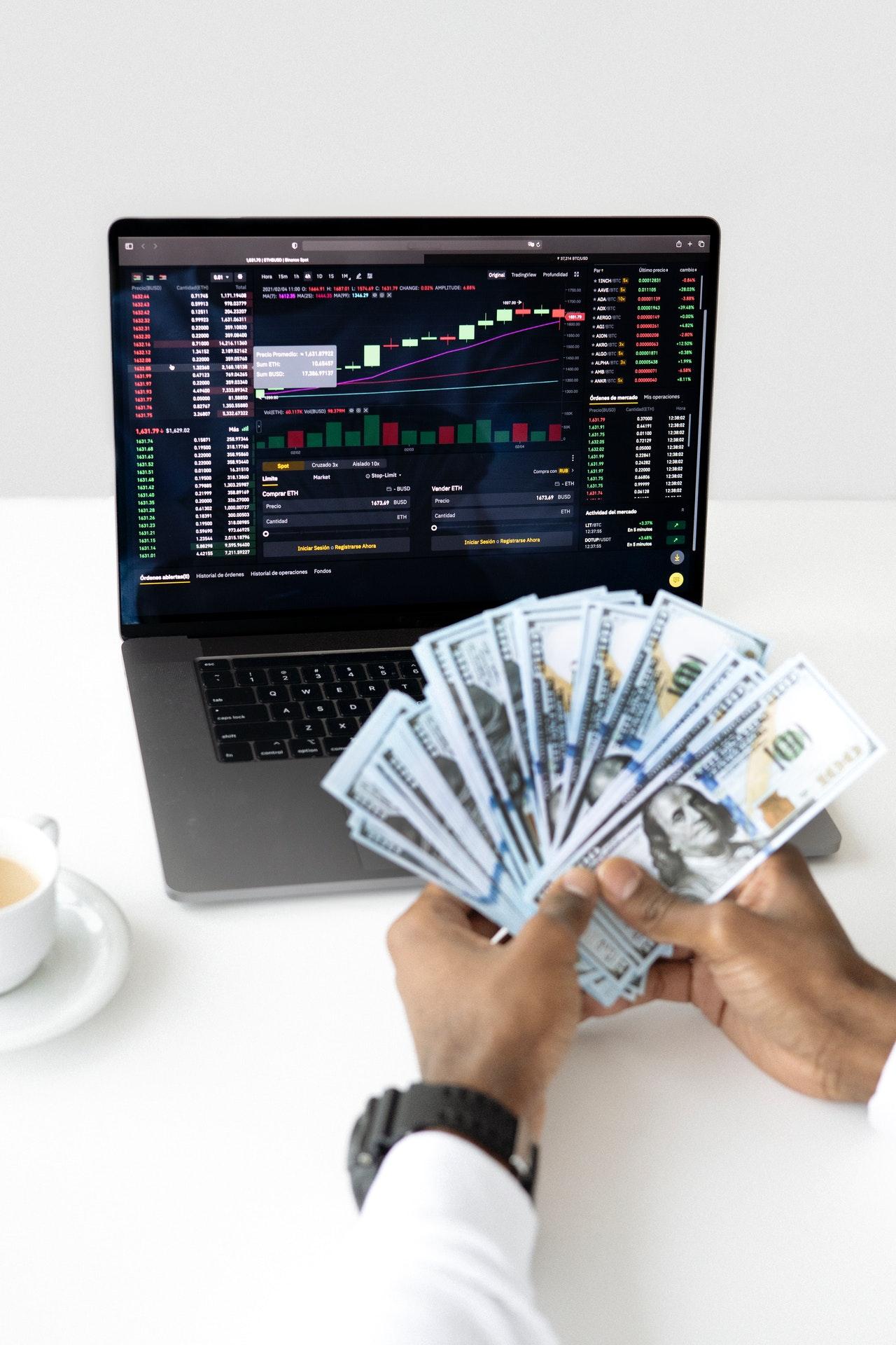 A person fanning cash in front of a computer screen