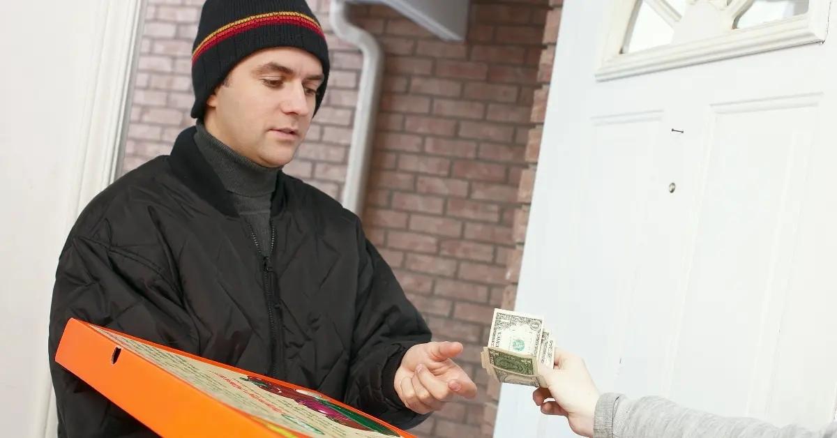 A pizza delivery guy in a black jacket collects his tip from a customer.