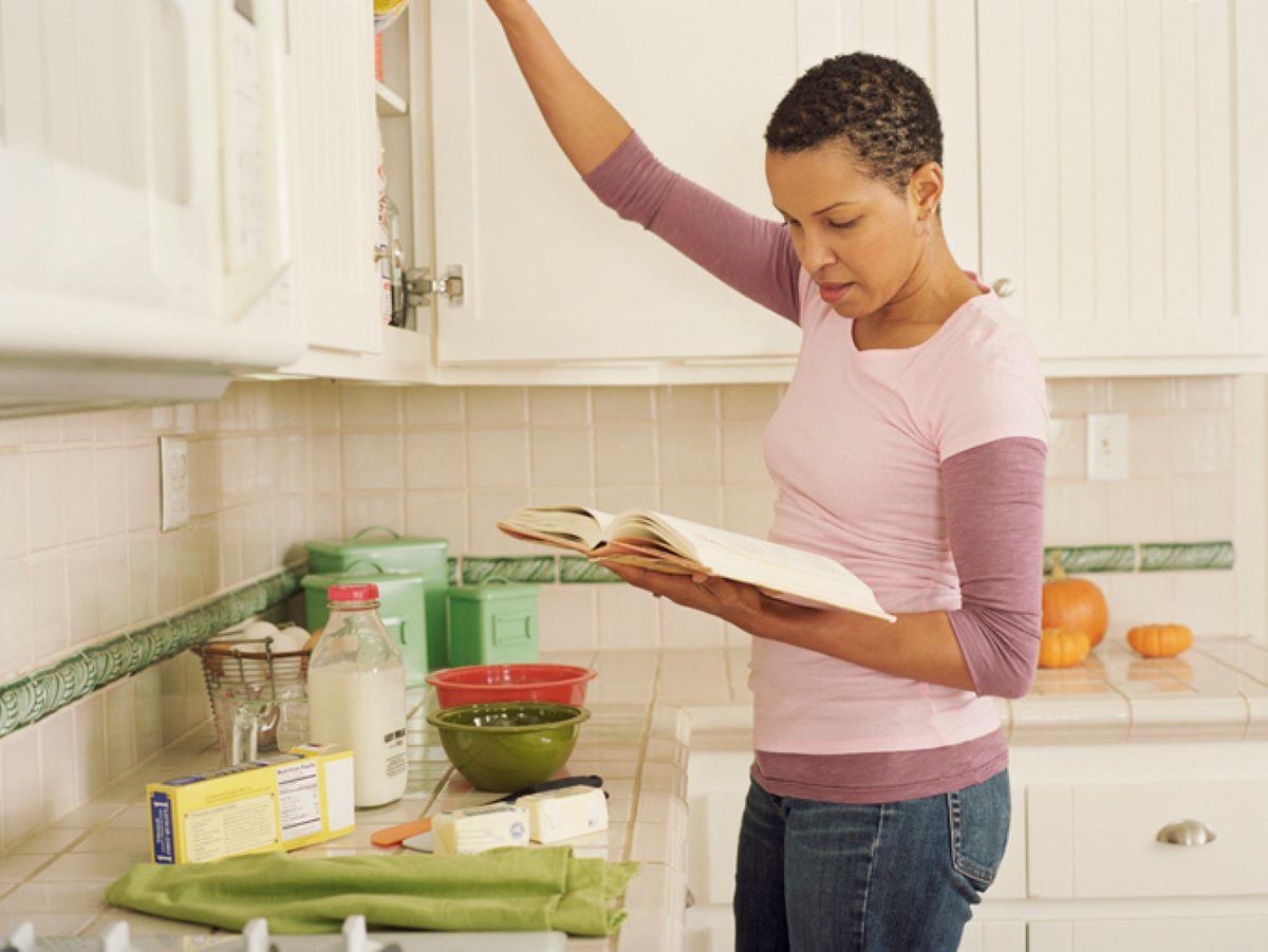 A woman in a kitchen looking at a cookbook