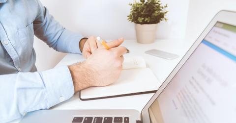 A person writing in a notebook beside a laptop