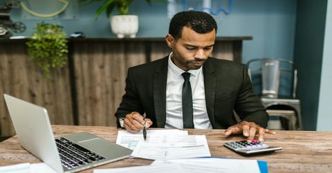 A person in a black suit working on a laptop and calculator