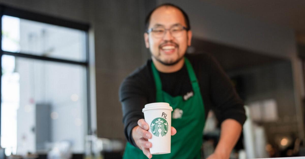 A Starbucks employee holding a pumpkin spice latte.