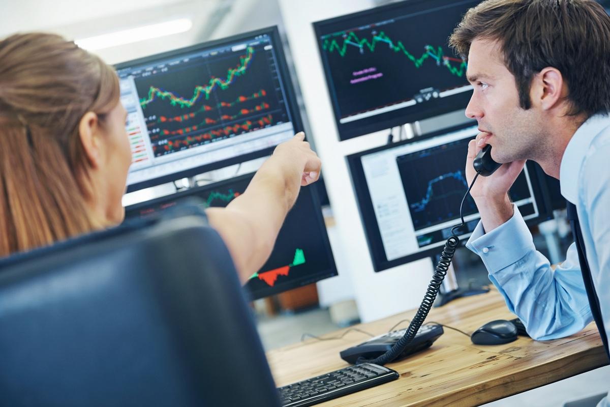 A rearview shot of two concerned stockbrokers looking at monitors displaying financial information