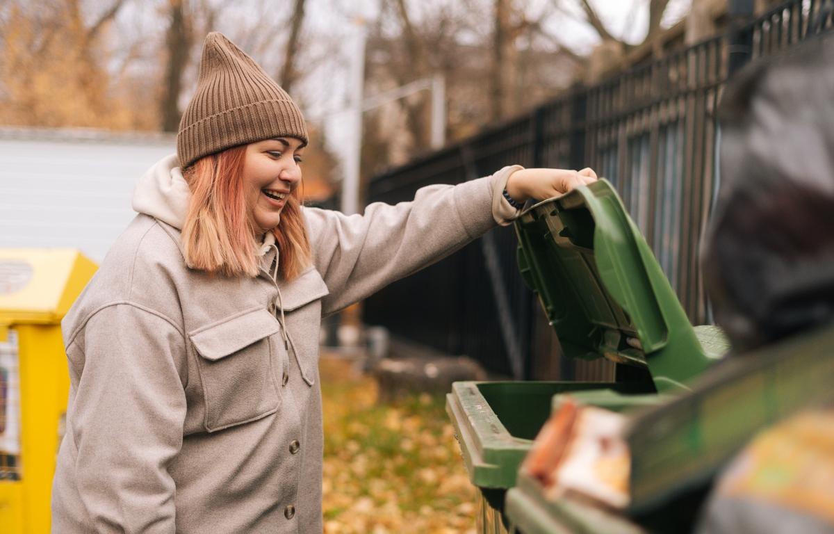 A woman in brown hat looking in a dumpster