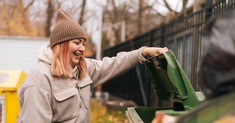 A woman in brown hat looking in a dumpster