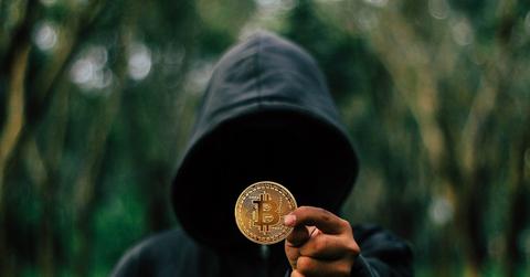 Person in a dark hoodie holding Bitcoin