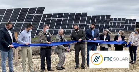 People at a ribbon cutting ceremony with solar panels and FTC Solar logo