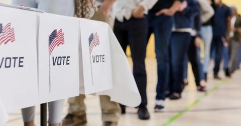 People stand in line behind a table with "vote" signs.