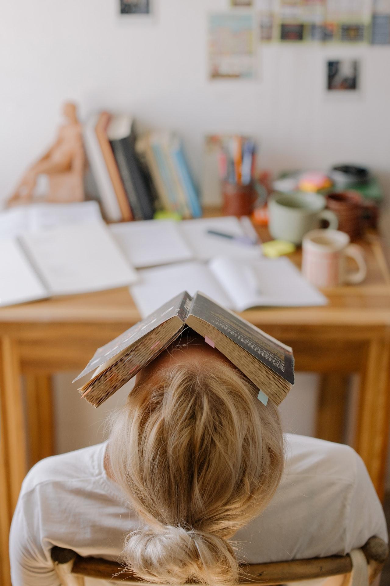 A student sitting in a library with a book over their face