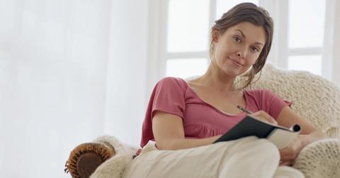 A smiling woman writing in a journal to sell on Amazon.