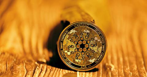 A black and gold Cardano coin is standing on a wood surface