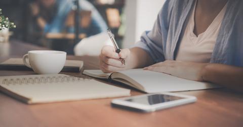 Person writing in notebook with coffee mug