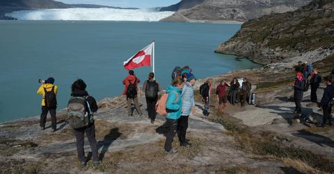 Tourists across from the Eqip Sermia glacier in Greenland with the Greenland national flag in the background.