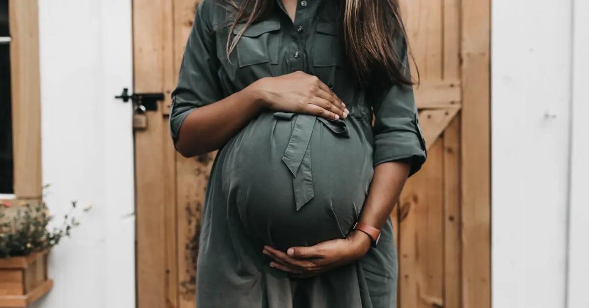 An expecting mother in a green green dress embracing her belly.