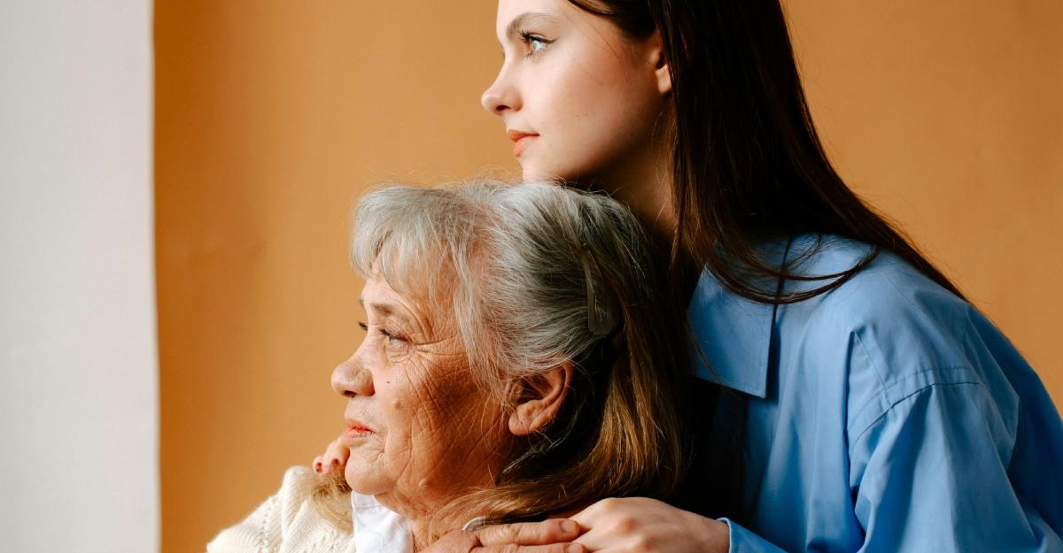 A young woman holds an older woman's shoulders as they look out the window.