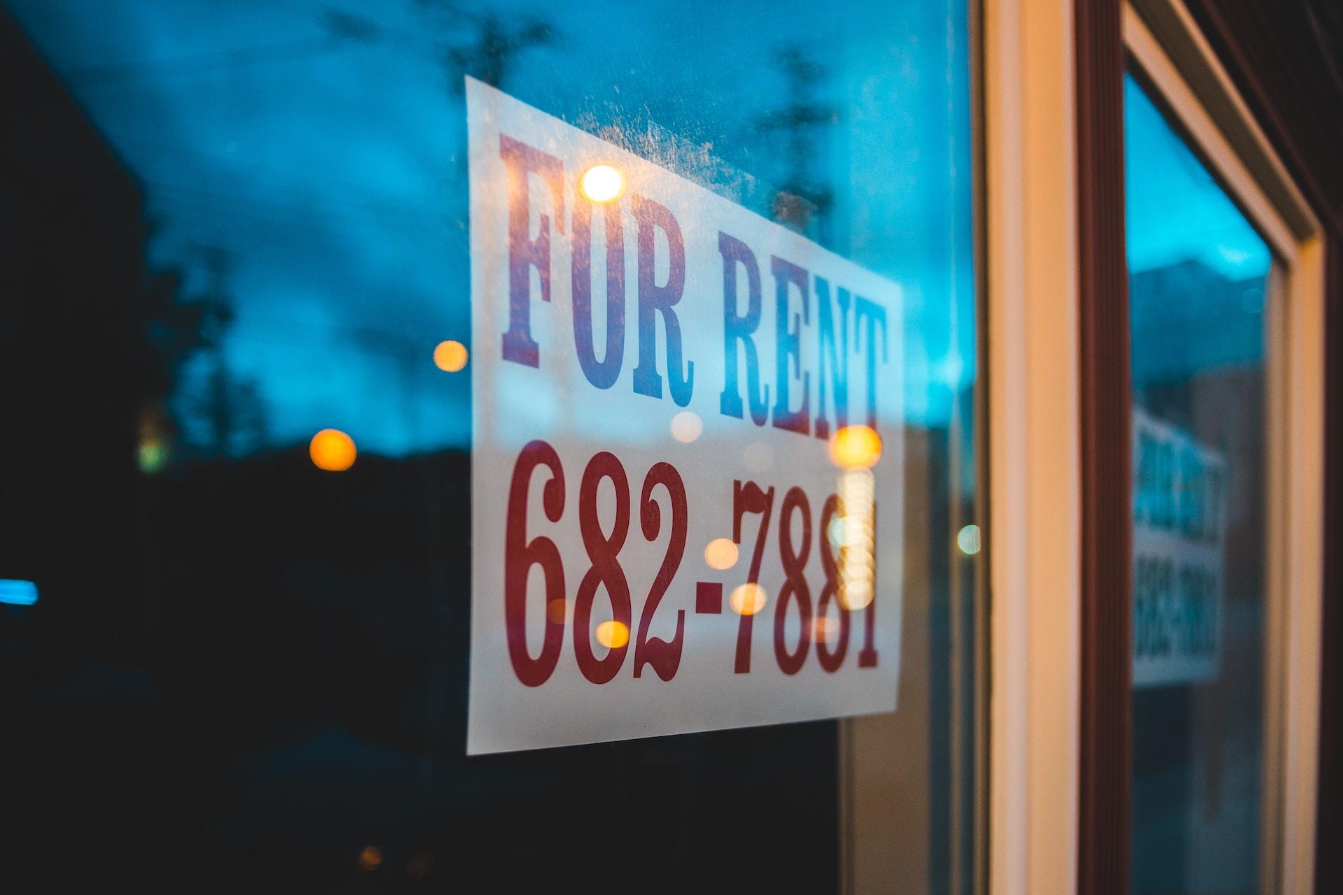 A "for rent" sign seen posted in a window reflecting lights off of it