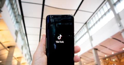 A person holding a smartphone displaying the TikTok logo