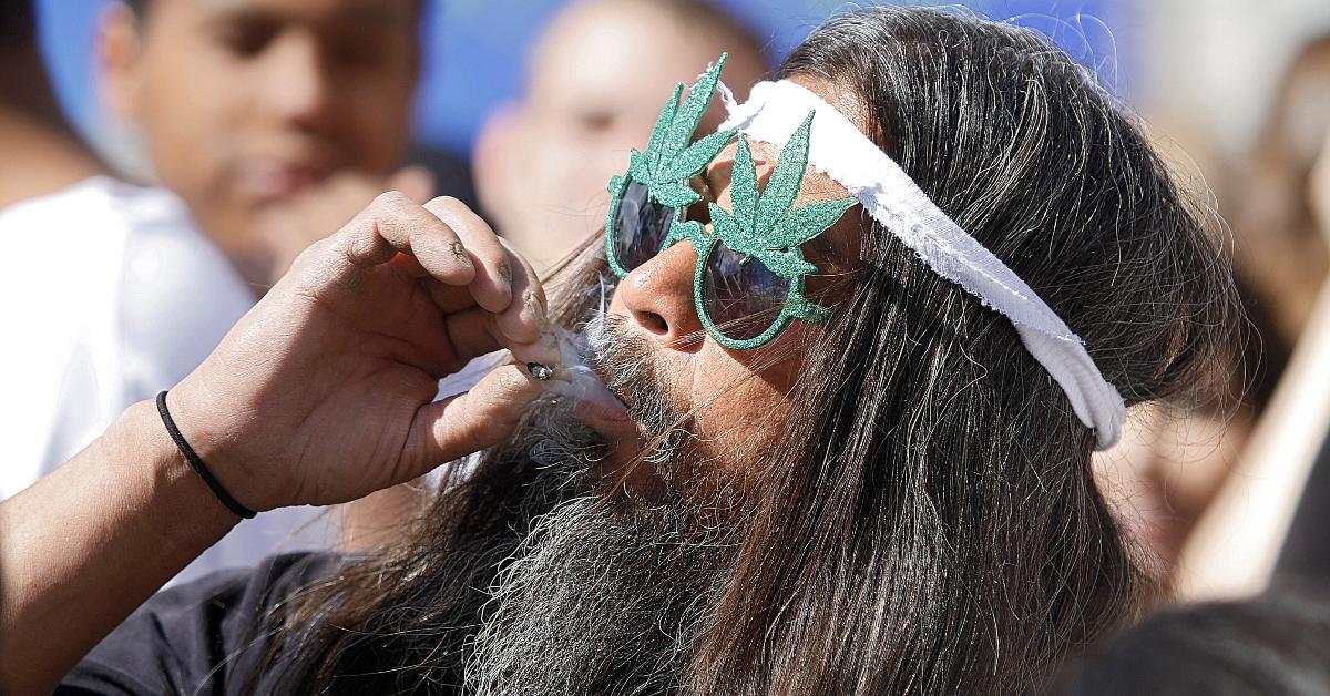 A man smoking a joint and wearing weed glasses.