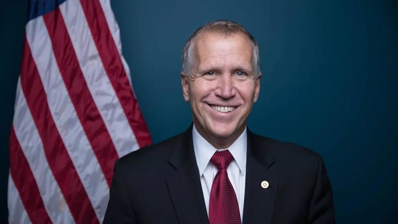 Senator Thom Tillis smiling in a dark suit with an American flag behind him