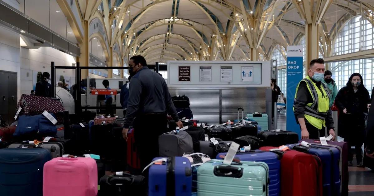 Airport workers surrounded by checked-in traveler baggage.