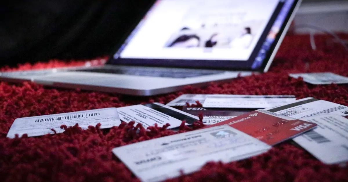 Several credit cards lay on a red carpet next to an open computer.