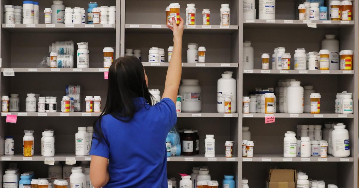 A drug store associate in blue reaches for amoxicillin.