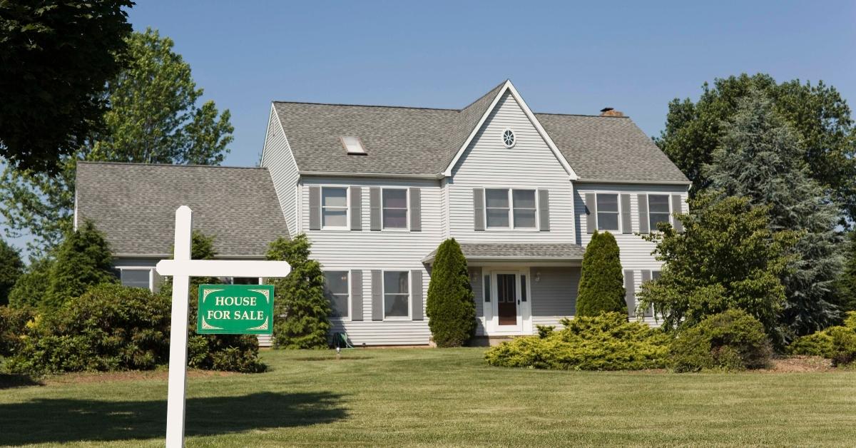 A for sale sign in front of a white and gray two-story house