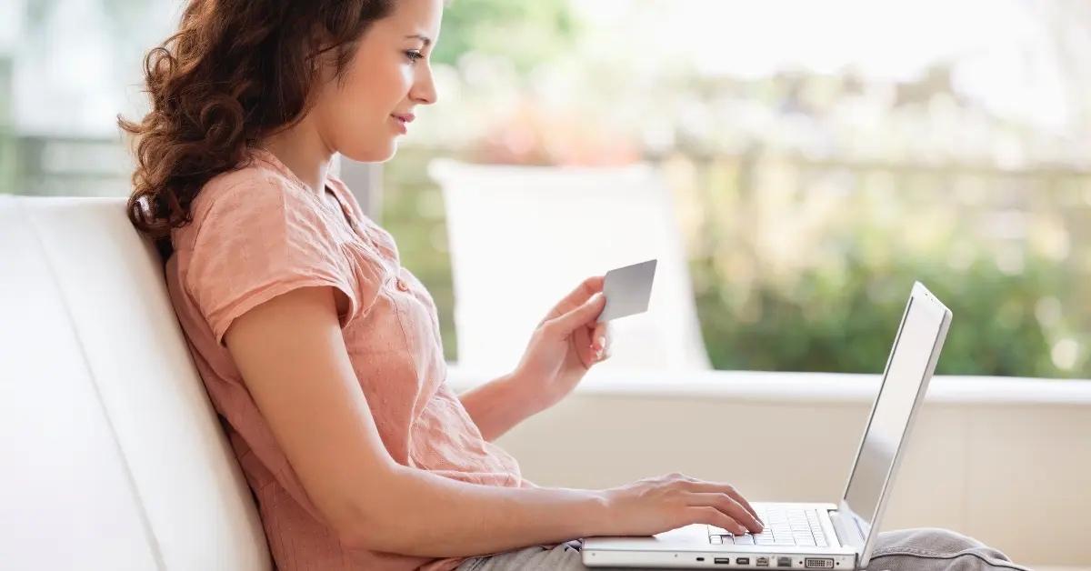 A happy woman in a pink shirt holding a credit card and requesting a limit increase on her computer.