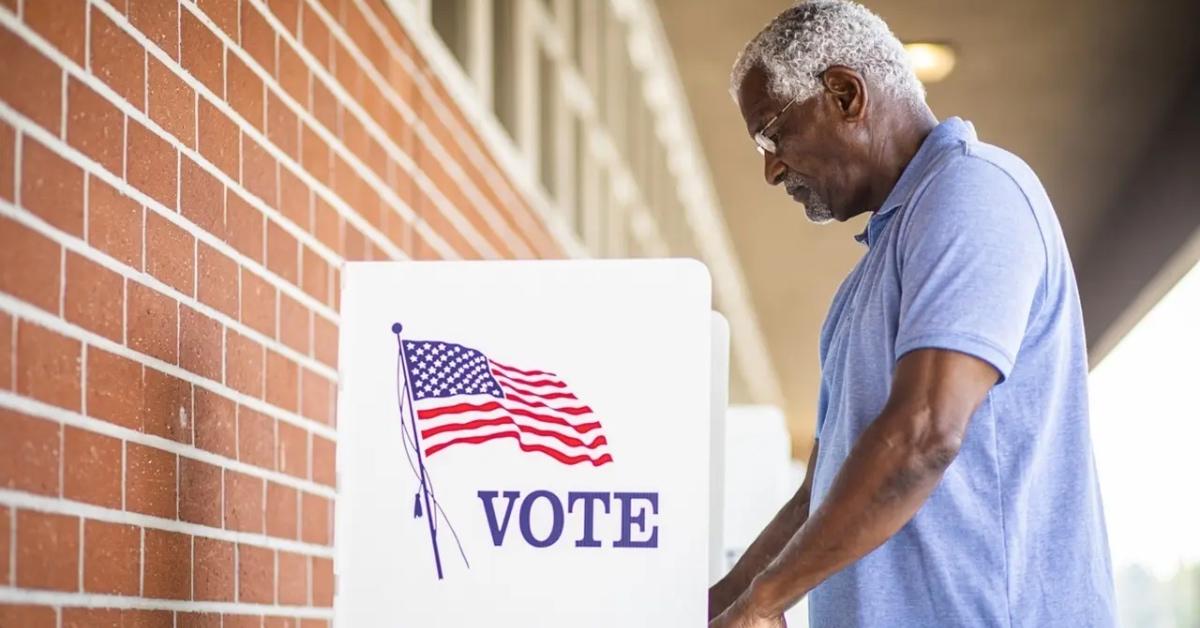 An elderly man in a blue shirt casts his vote in a private booth outside.