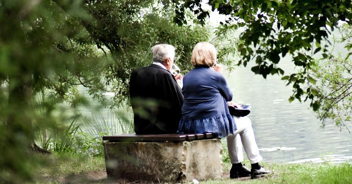 An older couple sitting by a lake enjoying a glass of wine.