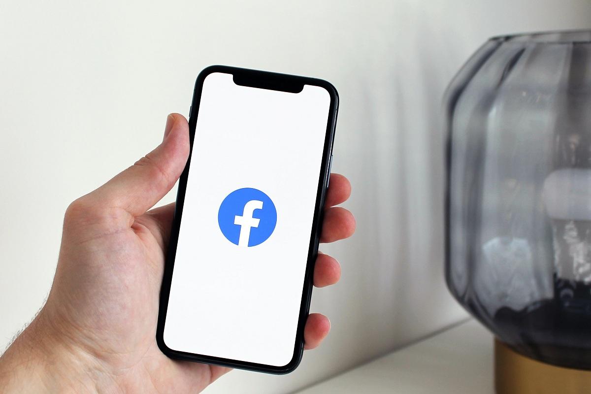 Person holding a smartphone displaying the Facebook logo