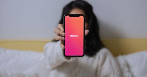 A woman holding a smartphone with the Tinder app on it