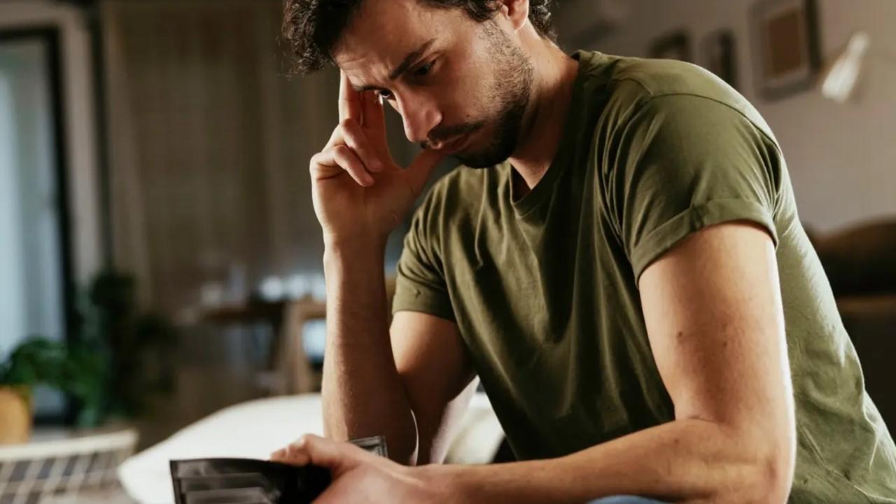 A worried man in green shirt holding an empty wallet