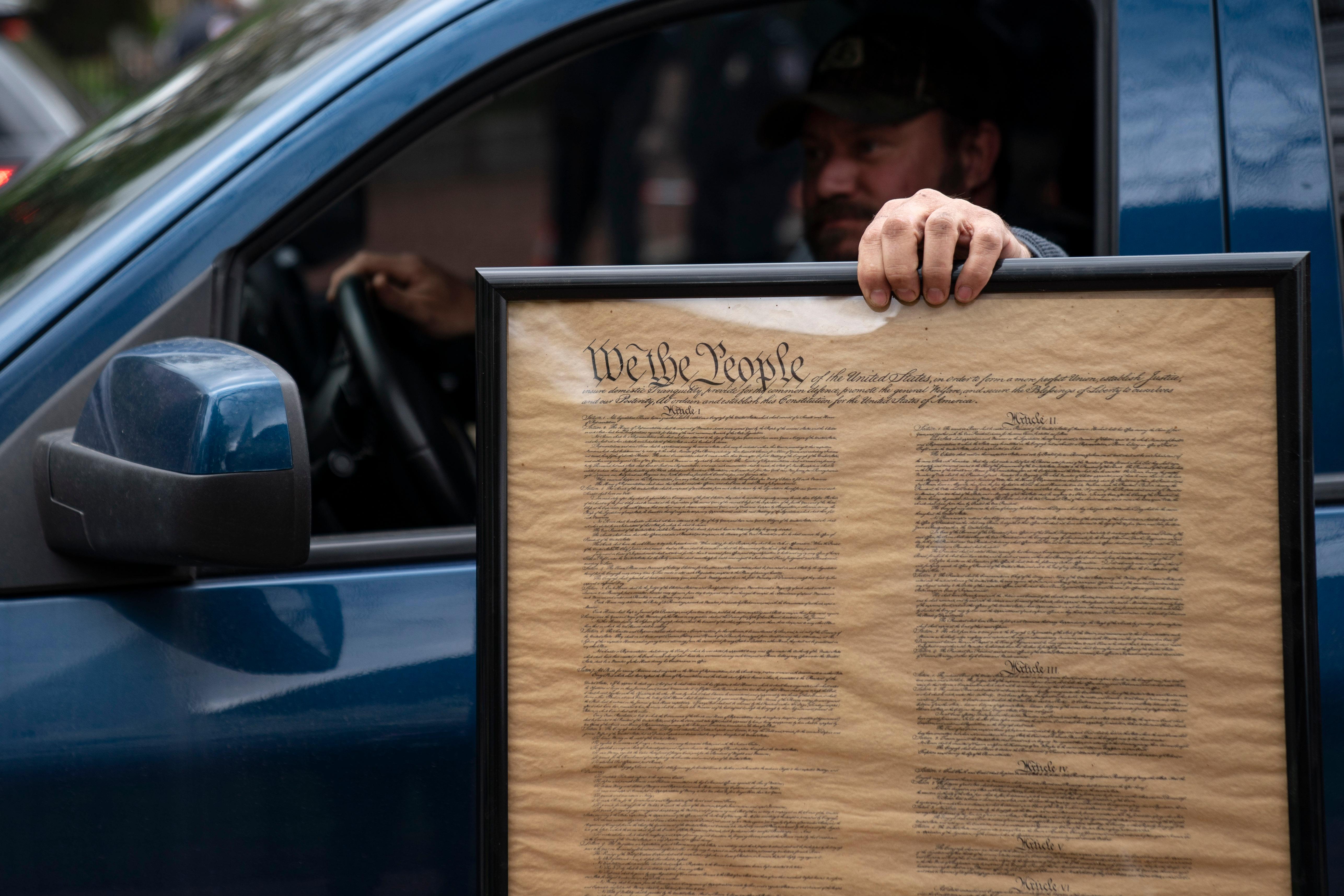 Man in car holding a framed copy of the U.S. Constitution