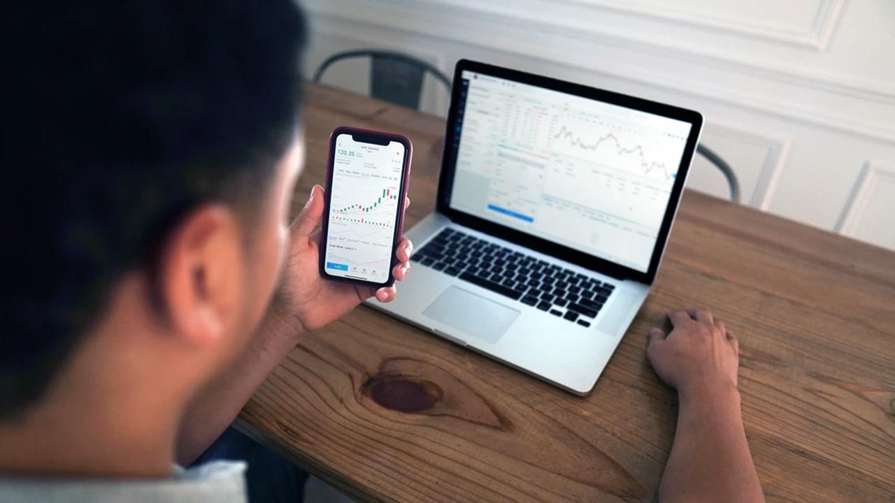 Man looking at stock data on a smartphone and laptop