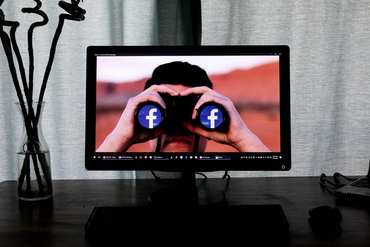 A man spying and holding Facebook binoculars on a computer screen