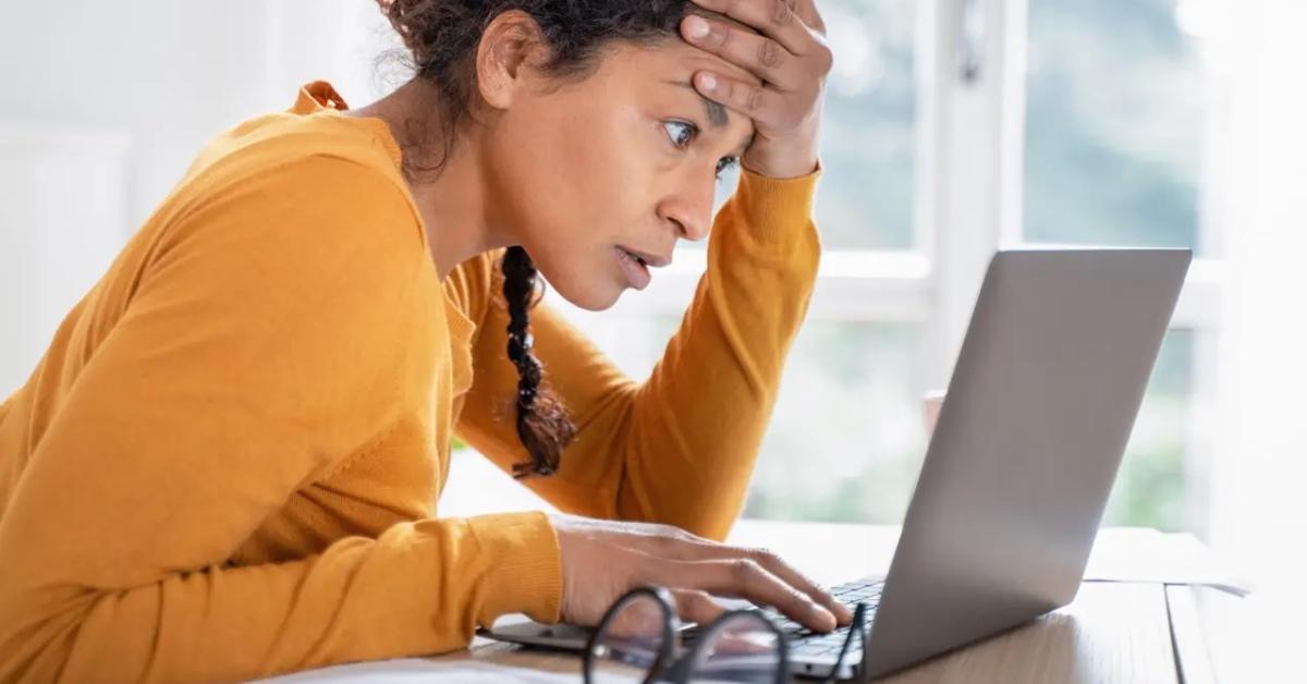 A stressed woman in a yellow shirt looking at taxes on her computer.