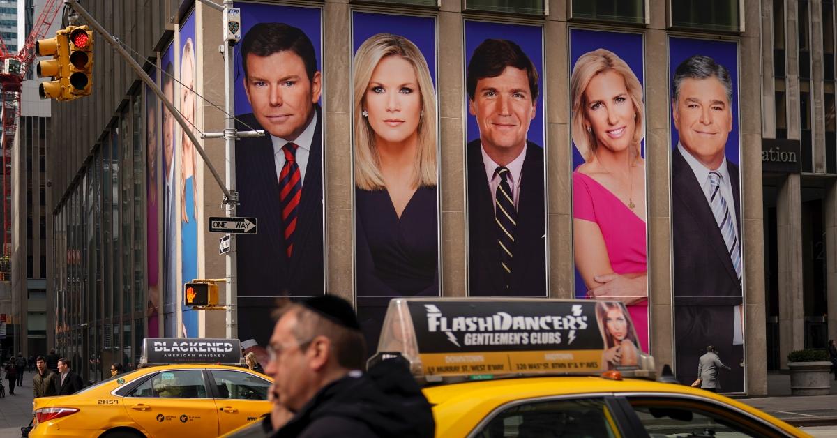 Traffic in New York City passes by a Fox News advertisement featuring personalities including Tucker Carlson