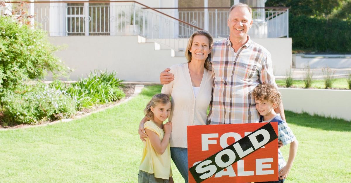 A family with a sold sign outside of a house