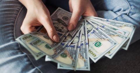 A woman holding a handful of $100 bills.